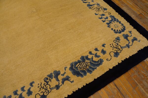 Gold rug with a medium pile features a dark blue floral and black border on wood flooring.