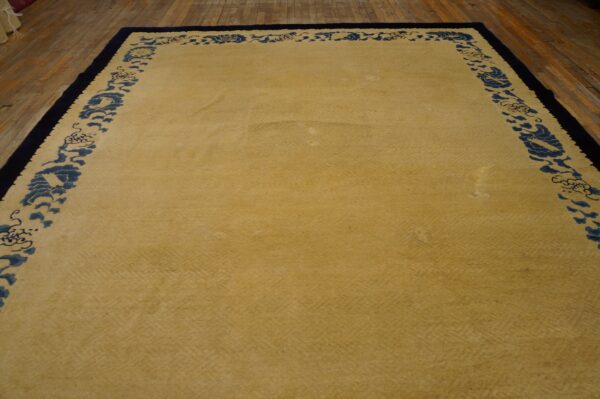 Yellow rug with subtle tonal field texture and blue stylized borders rests on rustic wood flooring.