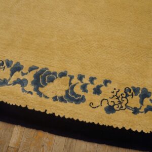 A textured golden rug field with a scalloped blue and black border resting on wood flooring.