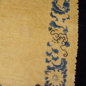 Plush yellow rug with blue stylized designs rests next to rustic orange wood flooring.