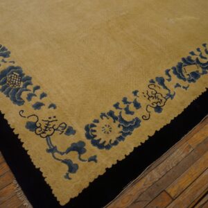 Tan rug with wide dark blue floral border and black edge rests on distressed wood flooring.