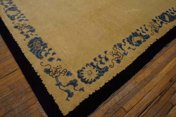 Tan rug with wide dark blue floral border and black edge rests on distressed wood flooring.