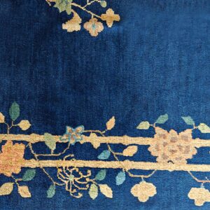 A close-up of a navy blue high-pile rug with a detailed gold, peach, and green floral border design.
