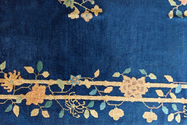 A close-up of a navy blue high-pile rug with a detailed gold, peach, and green floral border design.