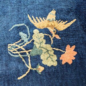 Detailed view of a deep blue high-pile rug featuring a golden bird and botanical design.