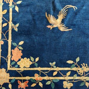 Deep blue rug detail showing a gold flying bird and a floral border of beige, peach, and green colors.