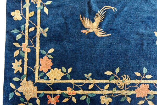 Deep blue rug detail showing a gold flying bird and a floral border of beige, peach, and green colors.