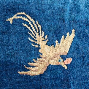 Textured blue rug detail with a cream-colored stylized flying bird pattern.