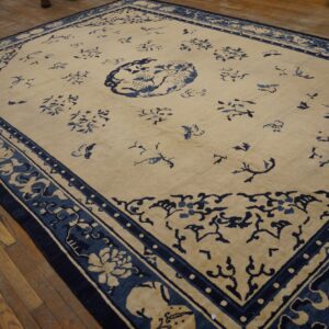 Pale beige rug with a blue central medallion and detailed border on worn wooden flooring.