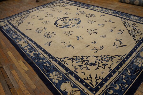 Pale beige rug with a blue central medallion and detailed border on worn wooden flooring.