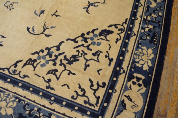 Beige rug corner featuring complex dark blue floral and scrollwork designs, resting on distressed hardwood flooring.