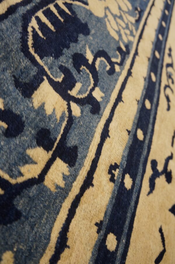 Close-up of a rug pattern featuring cream, dark blue, and variegated light blue pile textures.