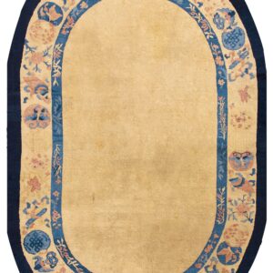 An oval tan rug featuring a decorative border with blue, peach, and navy traditional motifs.