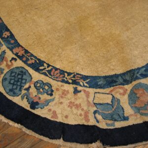 Round tan rug border with navy, light blue, and pink traditional motifs rests on wood floorboards.
