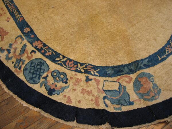 Round tan rug border with navy, light blue, and pink traditional motifs rests on wood floorboards.