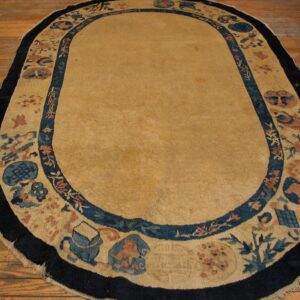 An oval tan rug with dark blue and coral border designs rests on warm hardwood flooring.