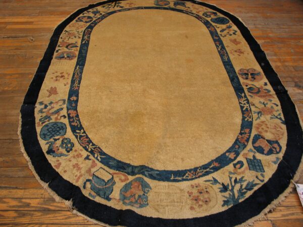 An oval tan rug with dark blue and coral border designs rests on warm hardwood flooring.