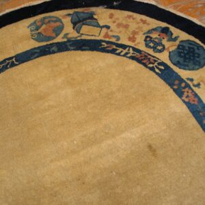 Curved view of a camel rug with intricate blue and terracotta borders over light wood flooring.