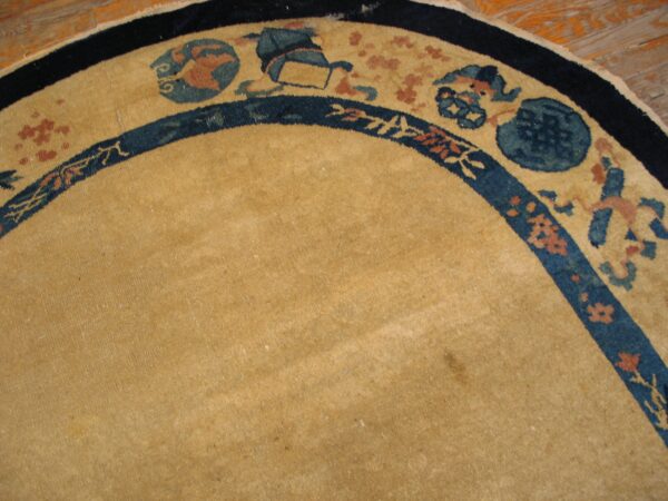 Curved view of a camel rug with intricate blue and terracotta borders over light wood flooring.