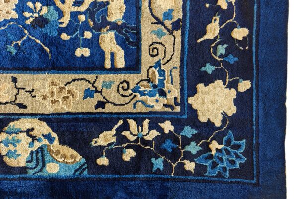 Corner detail of a plush rug in royal blue and beige with stylized floral motifs.