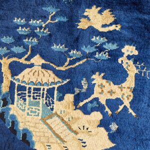 Close-up of a plush royal blue rug with a detailed beige and blue pattern showing a pavilion and deer.