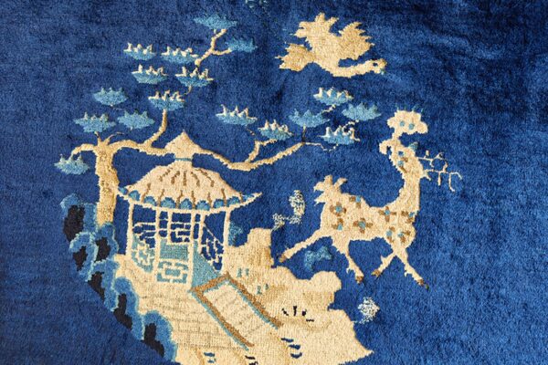Close-up of a plush royal blue rug with a detailed beige and blue pattern showing a pavilion and deer.