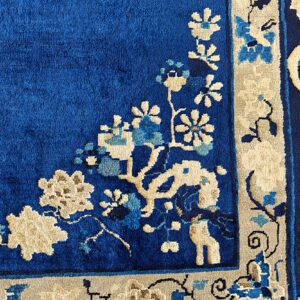 Detailed corner of a cobalt blue rug featuring an intricate beige and light blue floral border pattern.