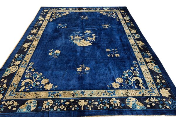 Deep blue rug featuring scattered tan florals, a central scenic medallion, and intricate bird-and-flower borders.