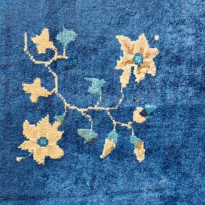 Close-up of a plush blue rug featuring a winding tan and aqua floral vine design.