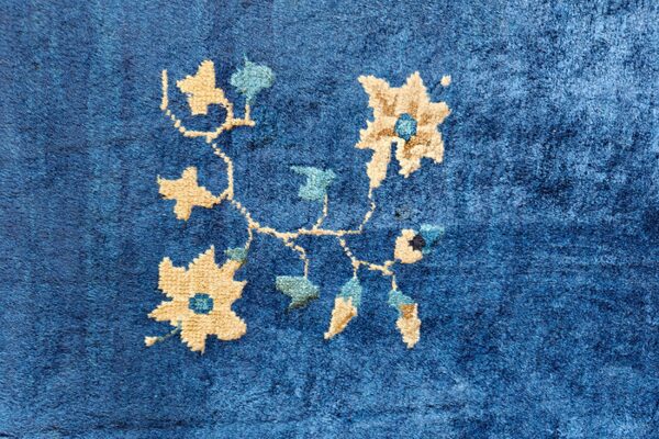 Close-up of a plush blue rug featuring a winding tan and aqua floral vine design.