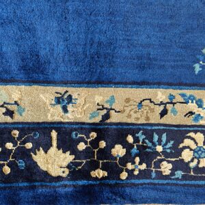 Plush blue rug texture showing tan and navy floral borders with scattered light blue accents.