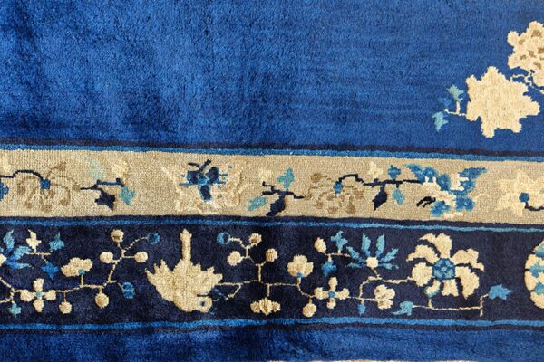 Plush blue rug texture showing tan and navy floral borders with scattered light blue accents.