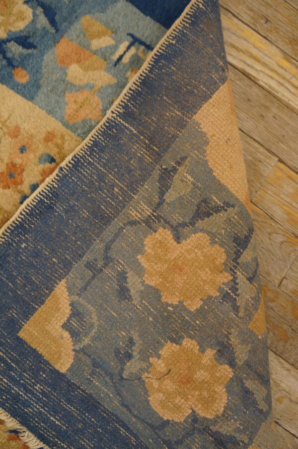 Floral blue rug, folded to expose its woven backing structure against distressed wooden planks.