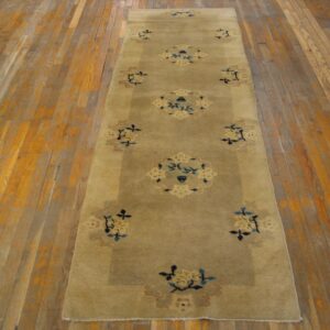A low-pile beige runner rug with blue and cream stylized floral medallions on distressed wood floor.