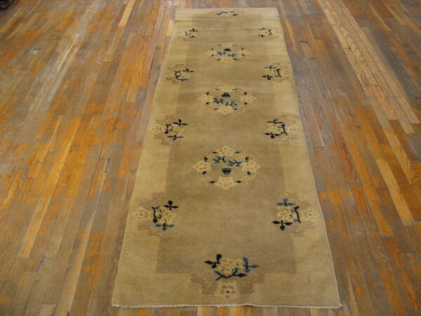 A low-pile beige runner rug with blue and cream stylized floral medallions on distressed wood floor.