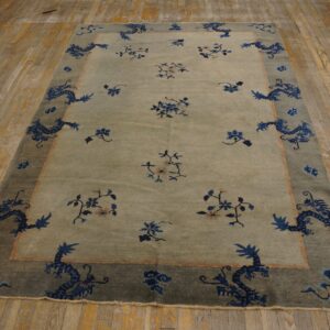 Pale green rug with a dark border features blue dragons and floral sprigs on distressed wood flooring.