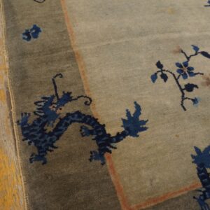 Low pile rug in sage and gray tones displays a navy dragon border next to distressed wood floor.