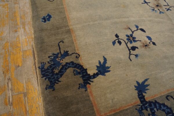 Low pile rug in sage and gray tones displays a navy dragon border next to distressed wood floor.