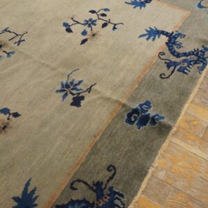 Beige rug with blue floral and stylized dragon patterns in a blue-grey border on wood planks.