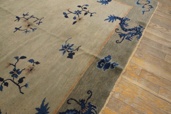 Beige rug with blue floral and stylized dragon patterns in a blue-grey border on wood planks.