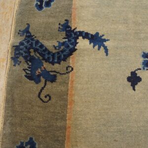 A blue dragon motif rug with a light gray-tan field lies against distressed wooden flooring.