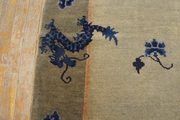 A blue dragon motif rug with a light gray-tan field lies against distressed wooden flooring.