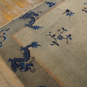 Muted blue-gray rug featuring a dark blue dragon border and florals lying on distressed wooden flooring.