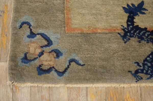 Muted green medium-pile rug with blue floral and dragon patterns bordered by orange, resting on wood floor.