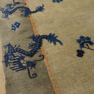 Khaki rug featuring distressed navy blue dragon and floral designs rests on natural wood planks.
