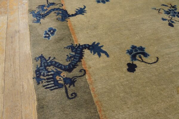 Khaki rug featuring distressed navy blue dragon and floral designs rests on natural wood planks.