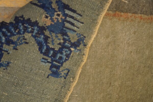 A folded rug shows a pixelated dark blue pattern on the sage pile next to a plain olive green texture.
