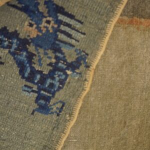 Detailed shot of a sage rug with blue patterns folded to reveal its tan woven backing.