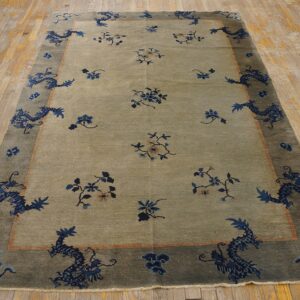Greenish-tan rug with indigo dragon and floral border displayed on light, worn wood flooring.