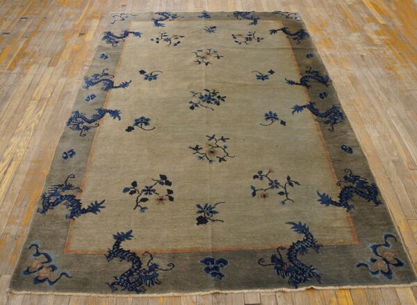 Greenish-tan rug with indigo dragon and floral border displayed on light, worn wood flooring.